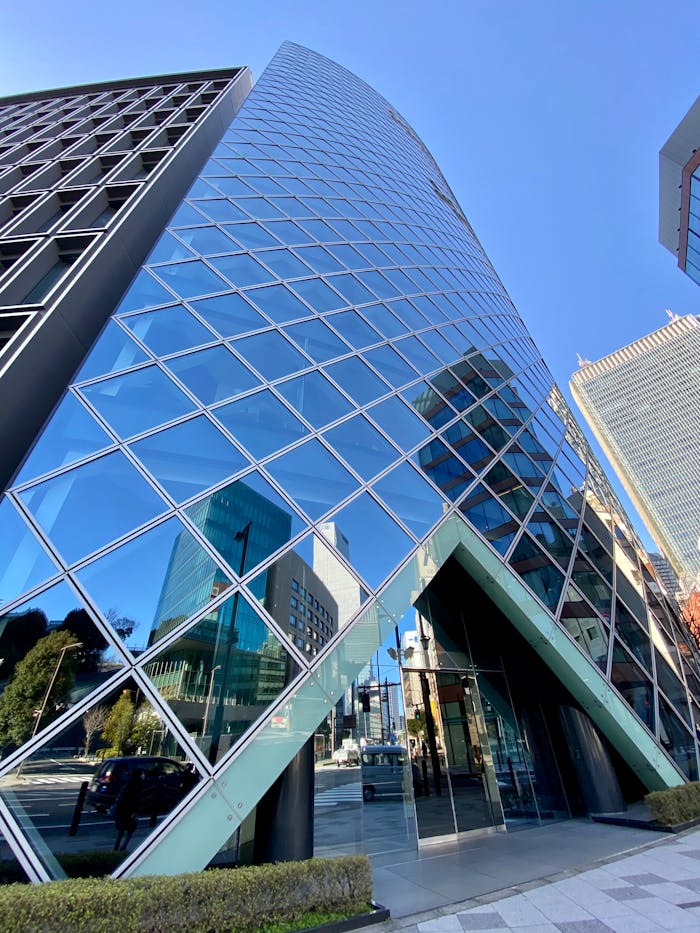Dramatic upward view of a modern glass skyscraper reflecting a vibrant cityscape.