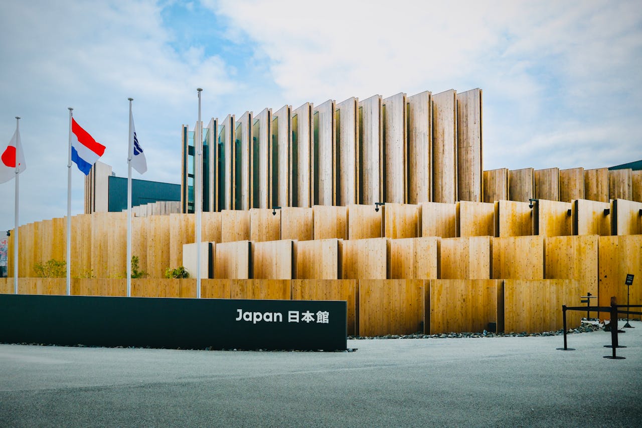 Striking wooden Japan Pavilion with flags waving under a vibrant sky, showcasing modern architectural design.